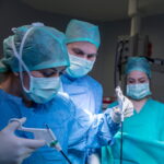 Een chirurgisch team voert geconcentreerd een minimaal-invasieve ingreep (kijkoperatie) uit in een modern uitgeruste operatiekamer. De focus ligt op precisie en specialistische zorg.