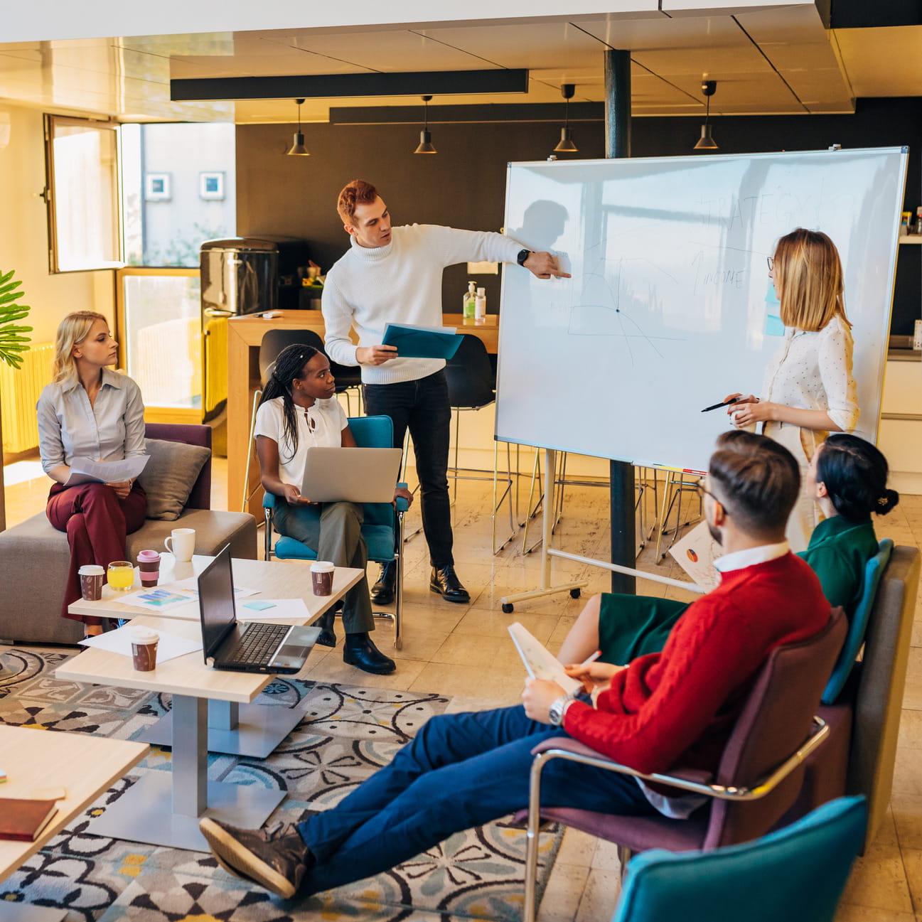 Een dynamisch team van professionals deelt ideeën en grafieken op een whiteboard tijdens een brainstormsessie in een modern, open kantoor. Samenwerking en creativiteit staan centraal.